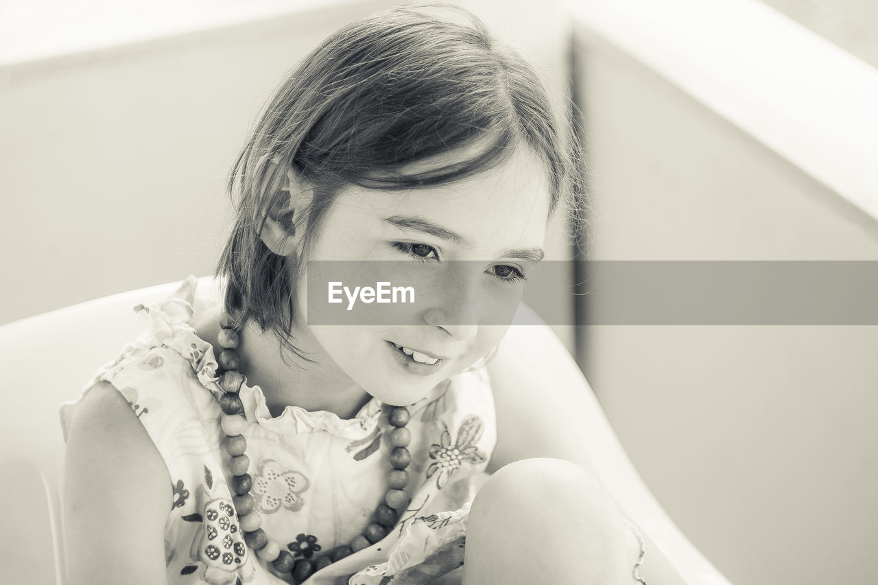 Smiling girl looking away while sitting against wall