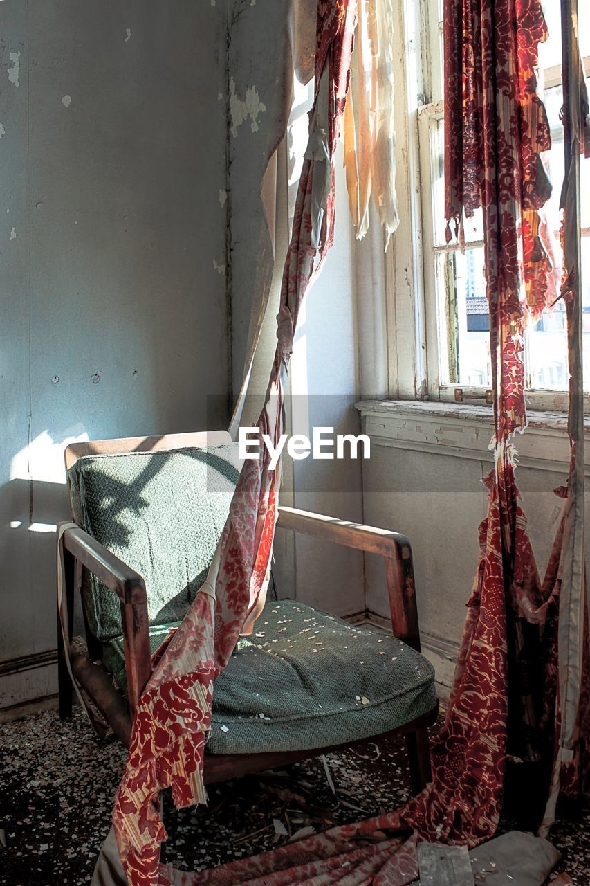 Torn curtains and old chair by window in abandoned room