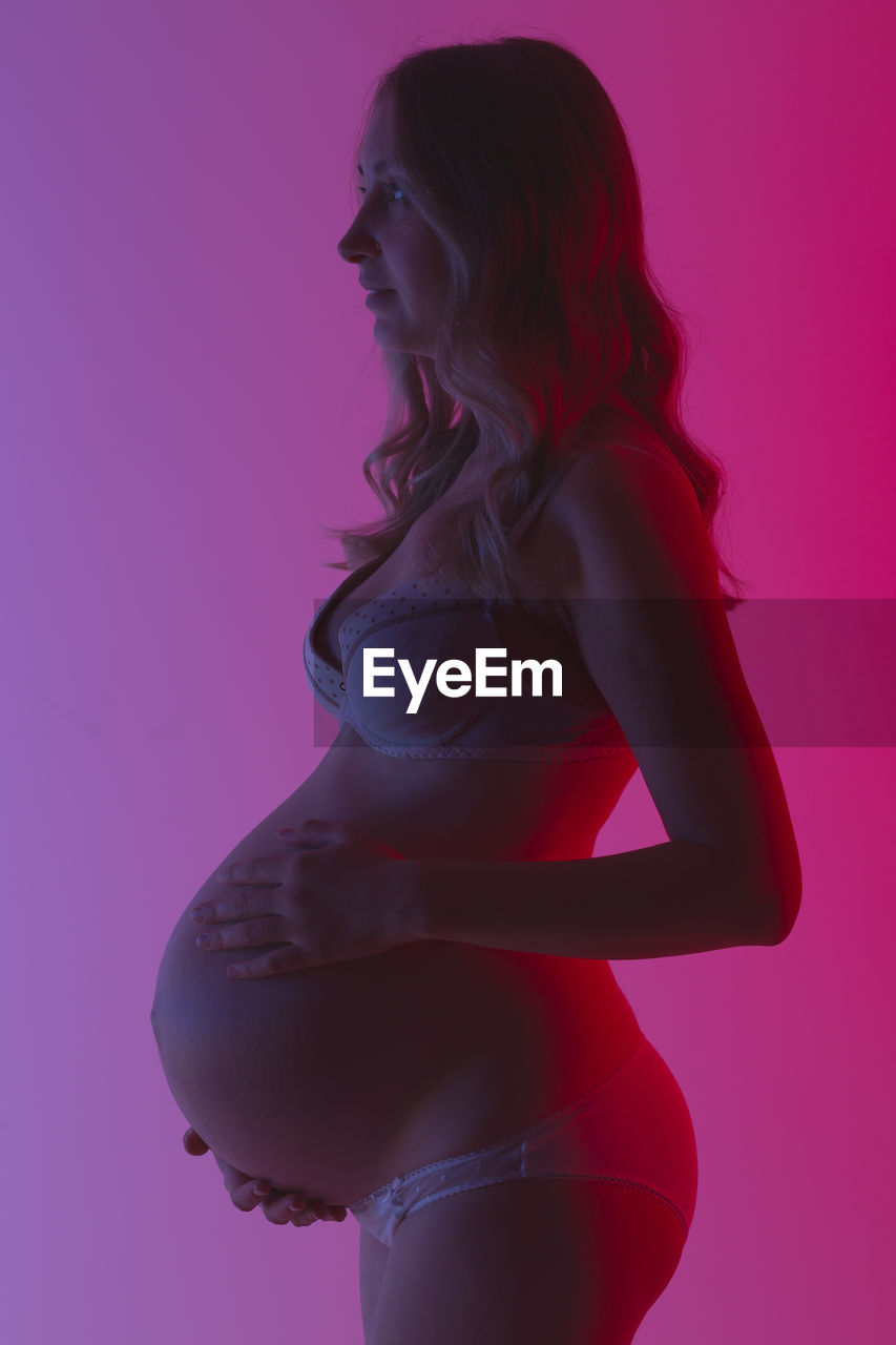 Pregnant woman standing against pink background