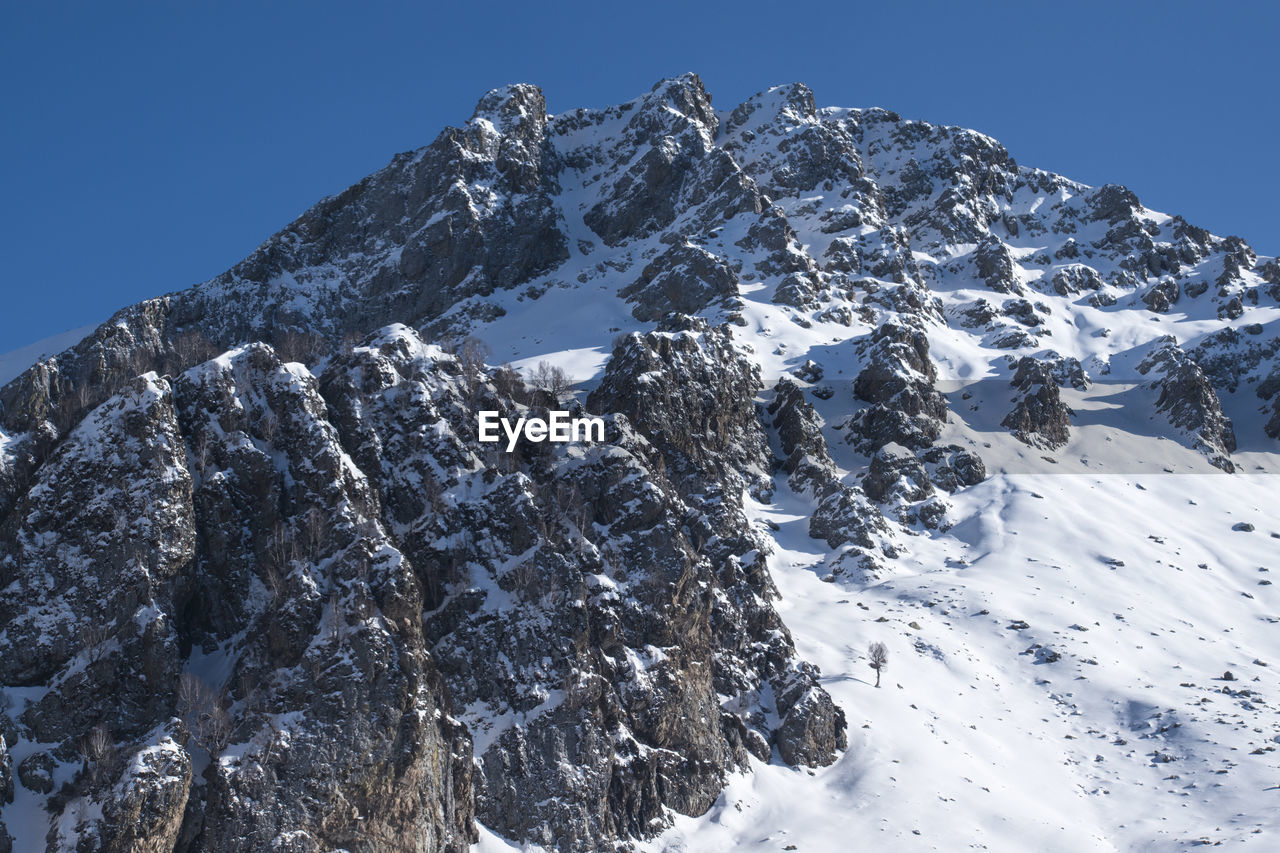 Low angle view of snowcapped mountains against clear blue sky