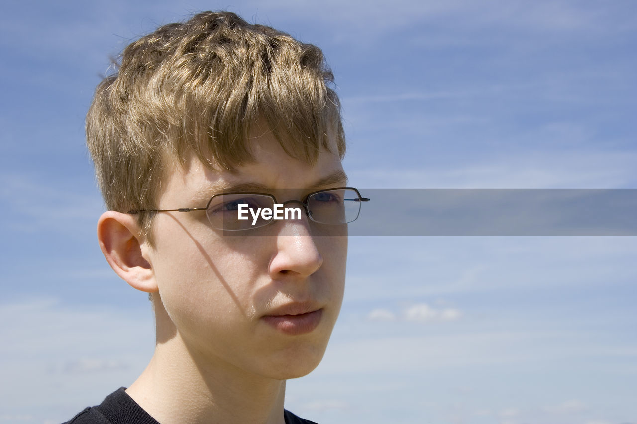 Close-up of thoughtful teenage boy wearing sunglasses while looking away against sky