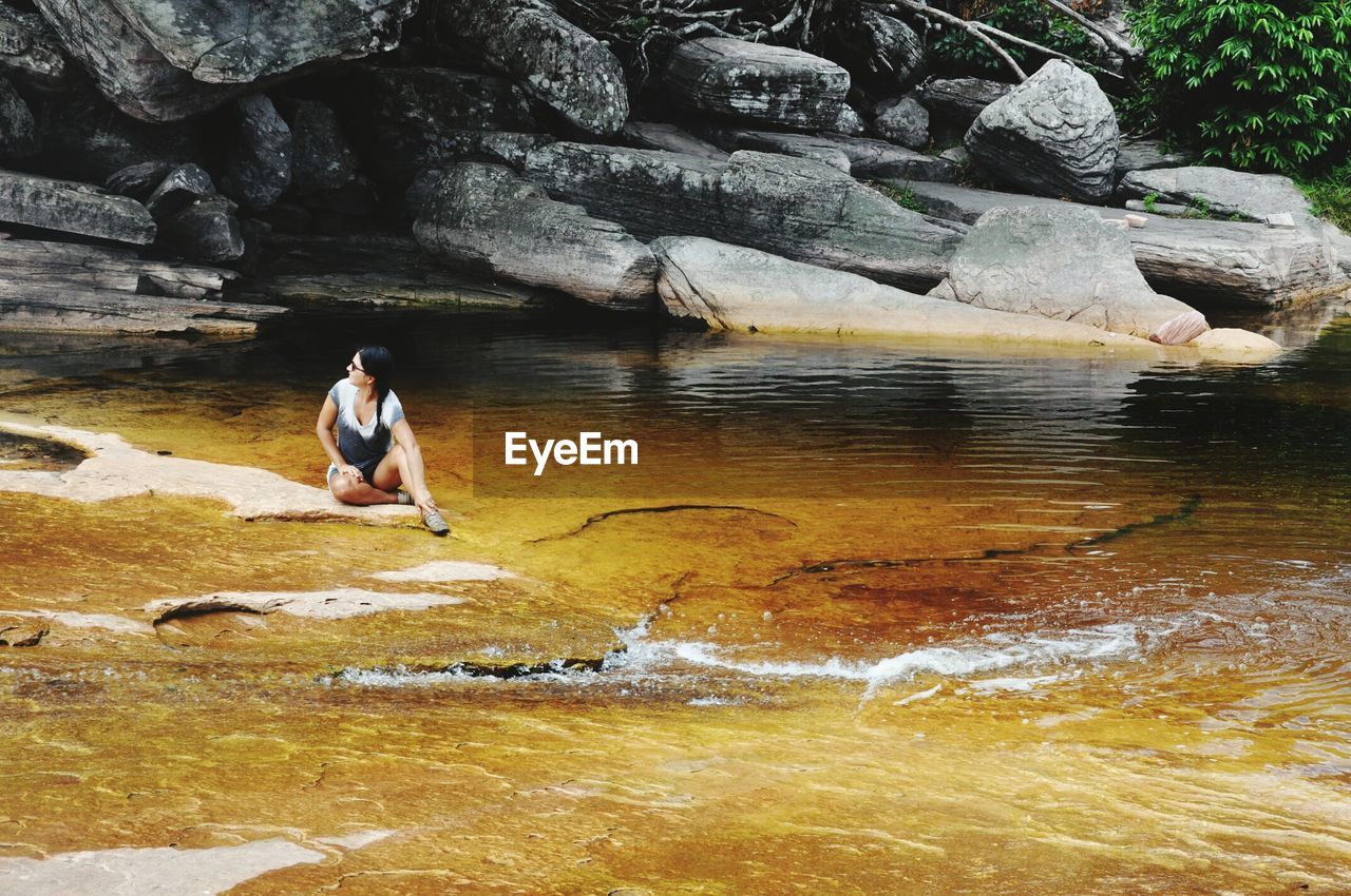 WOMAN SITTING BY ROCK FORMATION IN LAKE