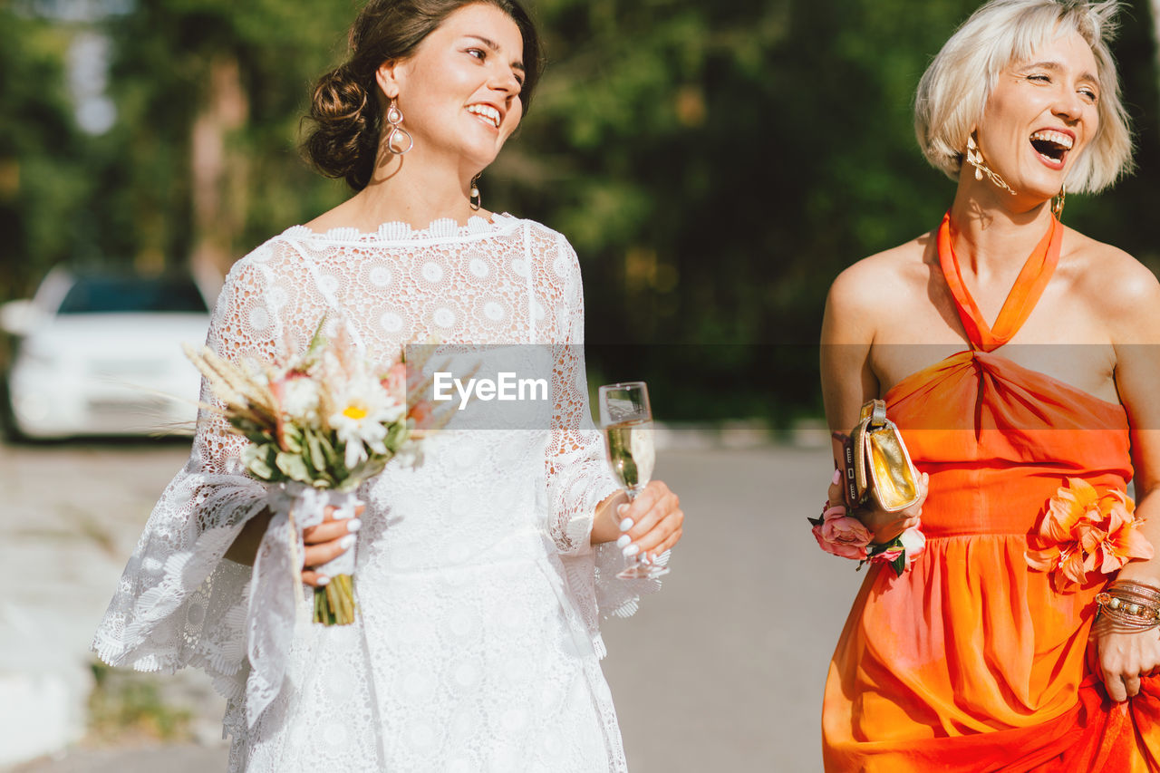 Smiling friends holding wine and bouquet on road