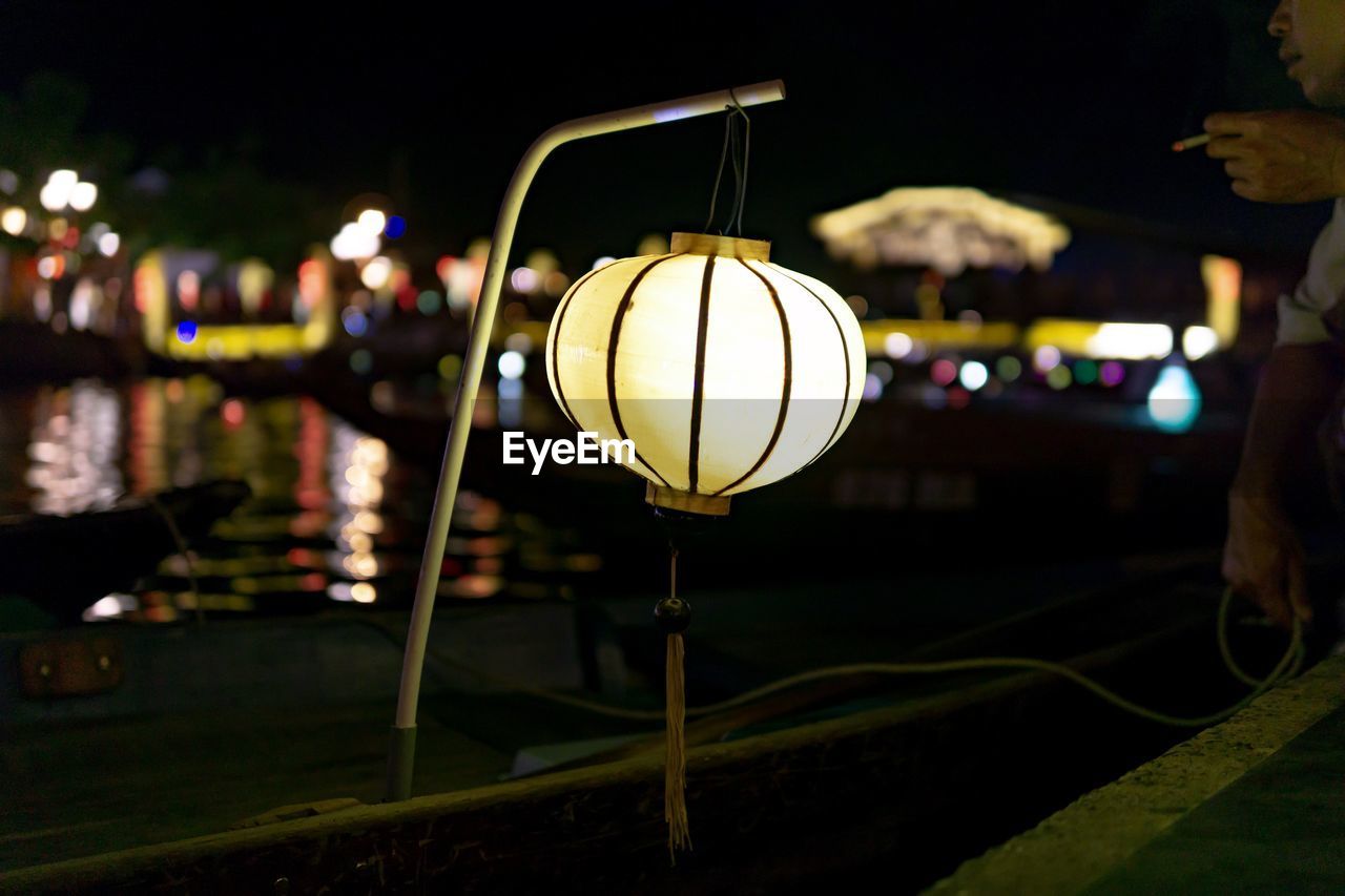 CLOSE-UP OF ILLUMINATED LIGHTS HANGING AT NIGHT