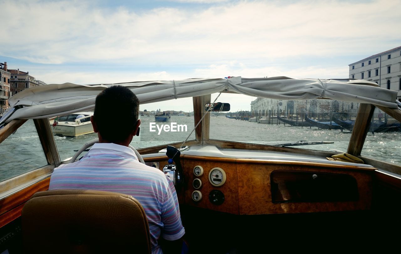 Rear view of man sitting on boat in sea against sky