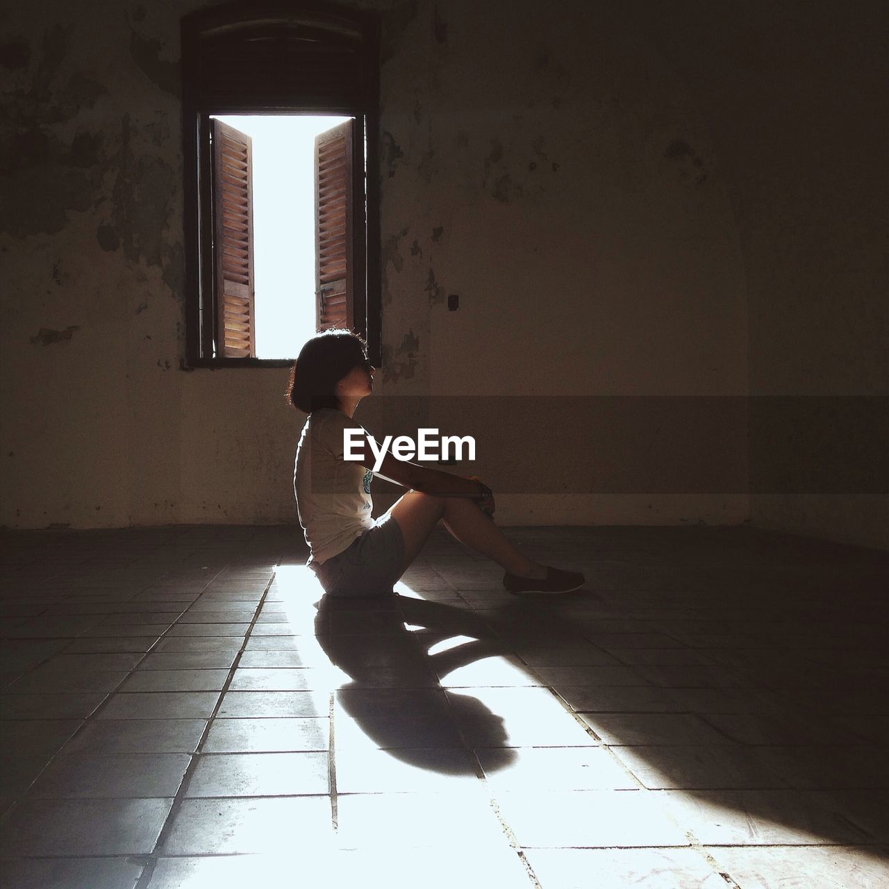 Full length side view of woman sitting in room against window