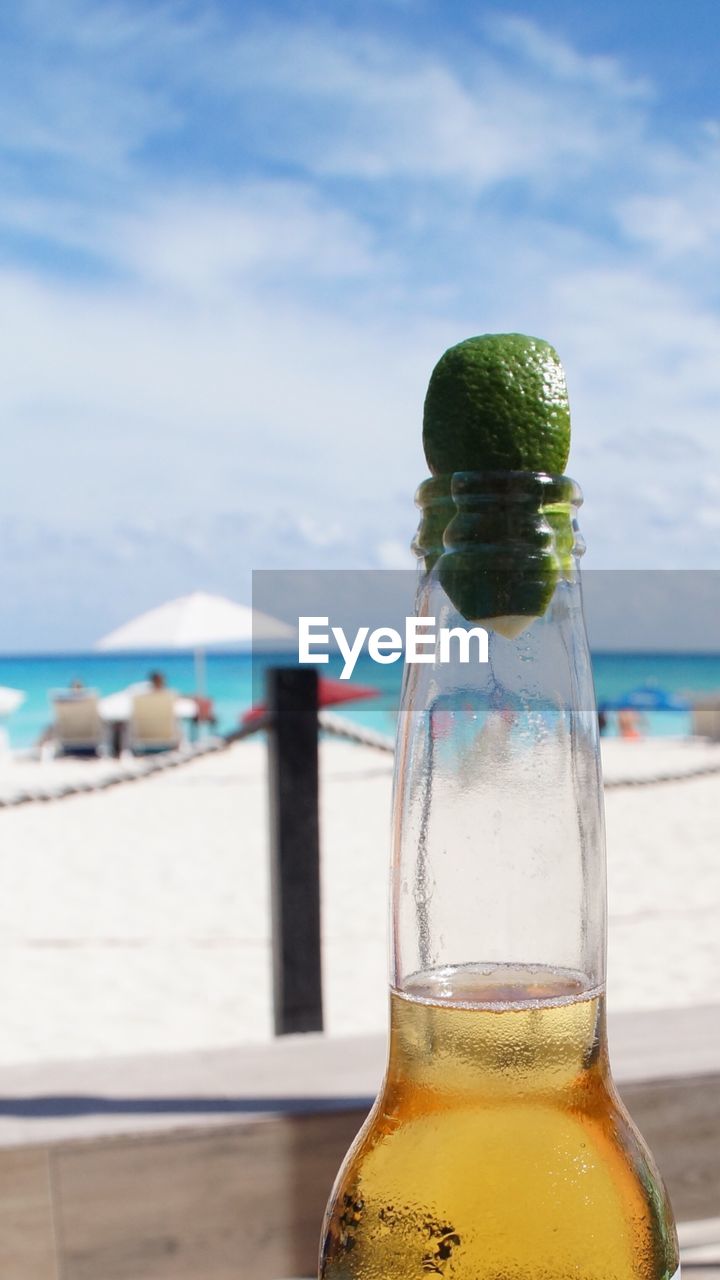 Close-up of beer bottle at beach against sky