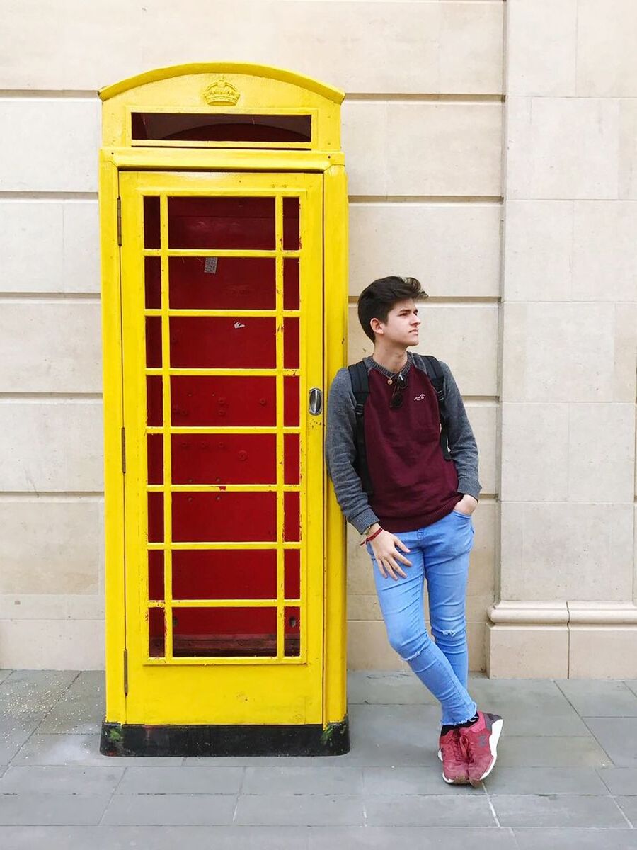 Young man leaning on telephone booth on footpath against building