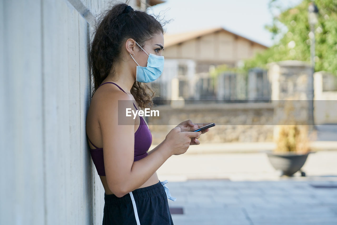 Woman in sportswear wearing a medical mask looking at a smartphone