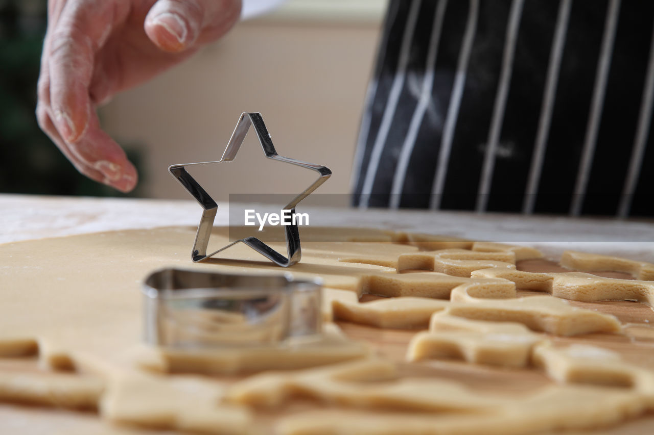 Cropped hands of chef cutting dough with pastry cutter at table