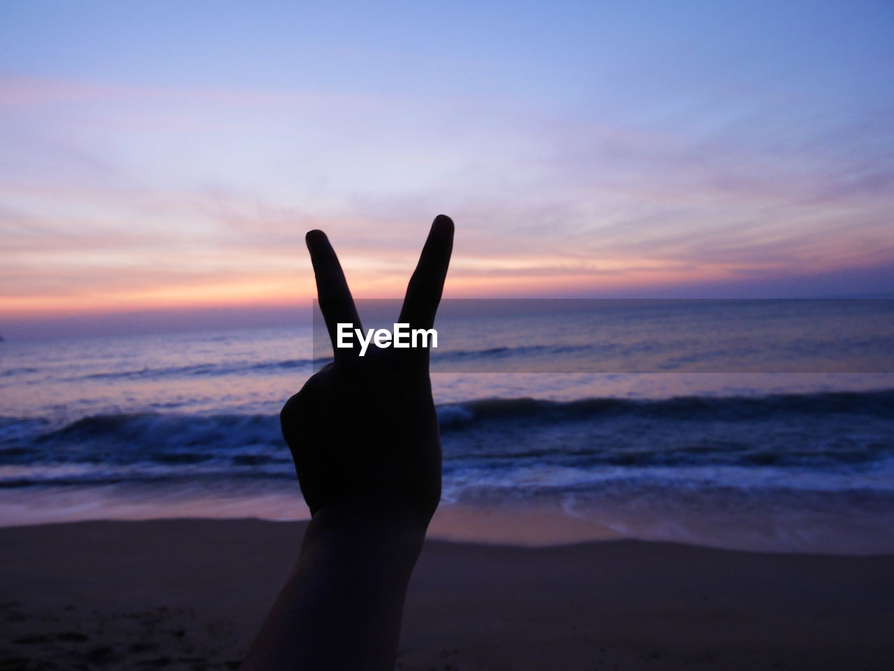 CLOSE-UP OF HAND BY SEA AGAINST SKY