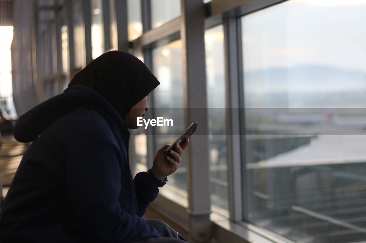 Woman wearing hijab while using mobile phone at airport