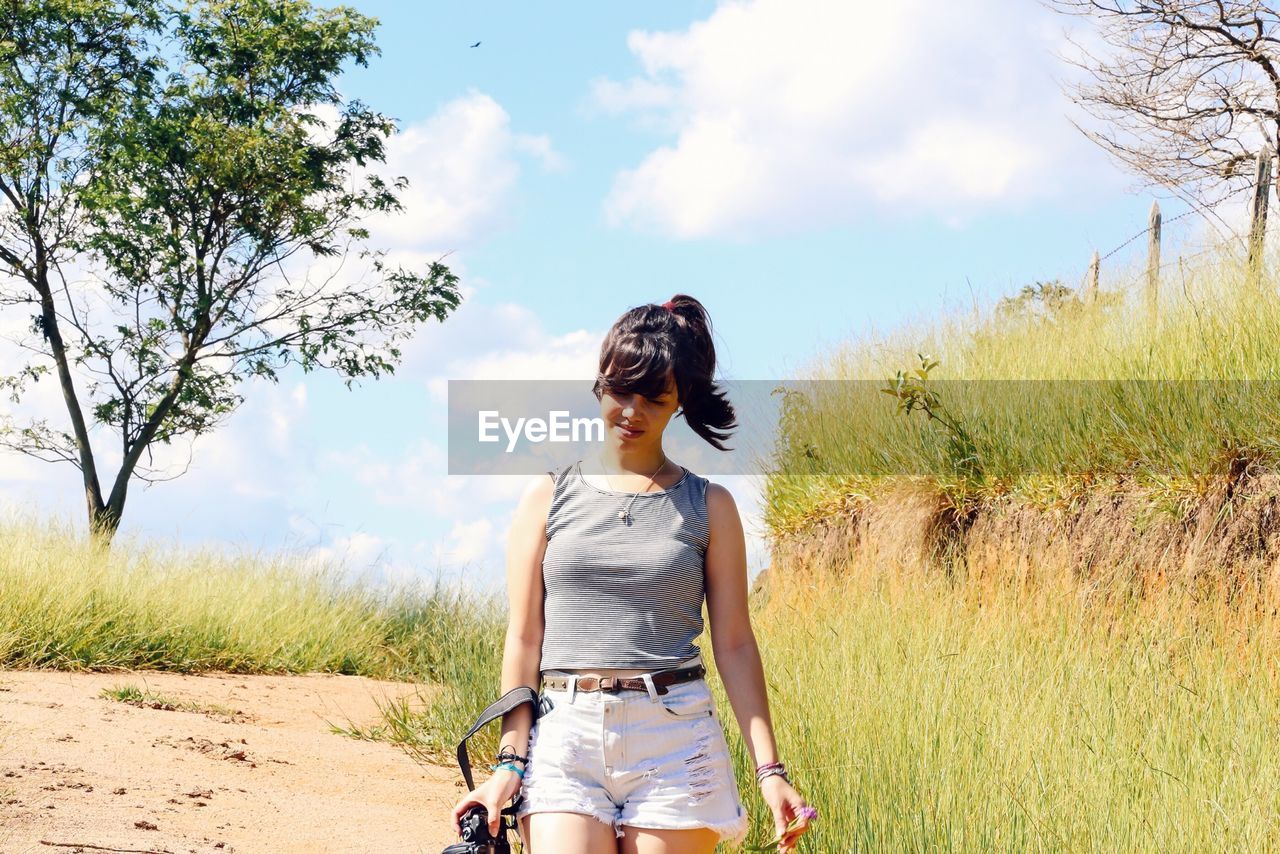 Young woman walking on field against sky