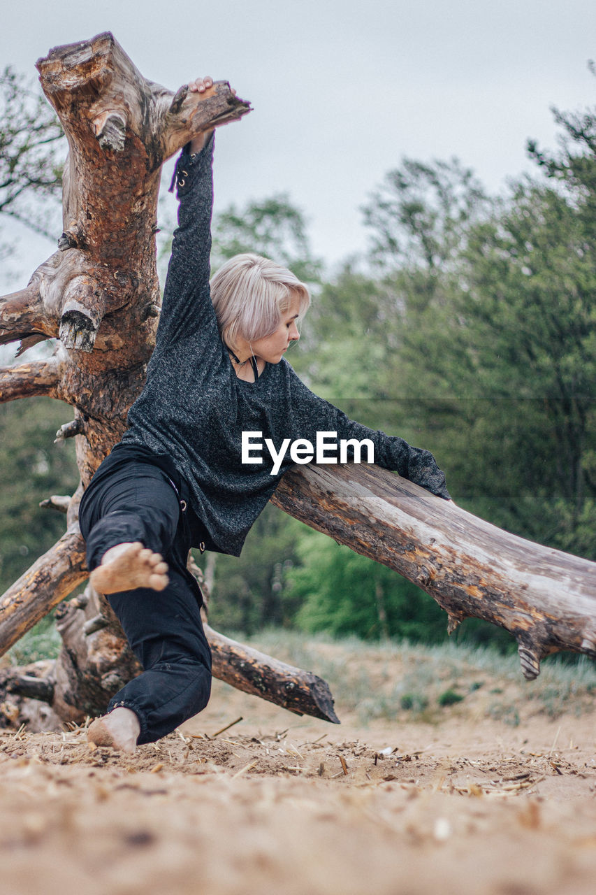 Full length of woman standing on fallen tree at forest