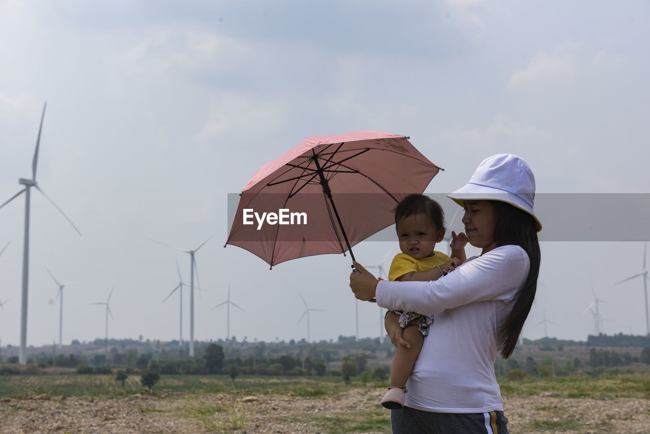 A young mother and her lovely little daughter are at a windmill field.