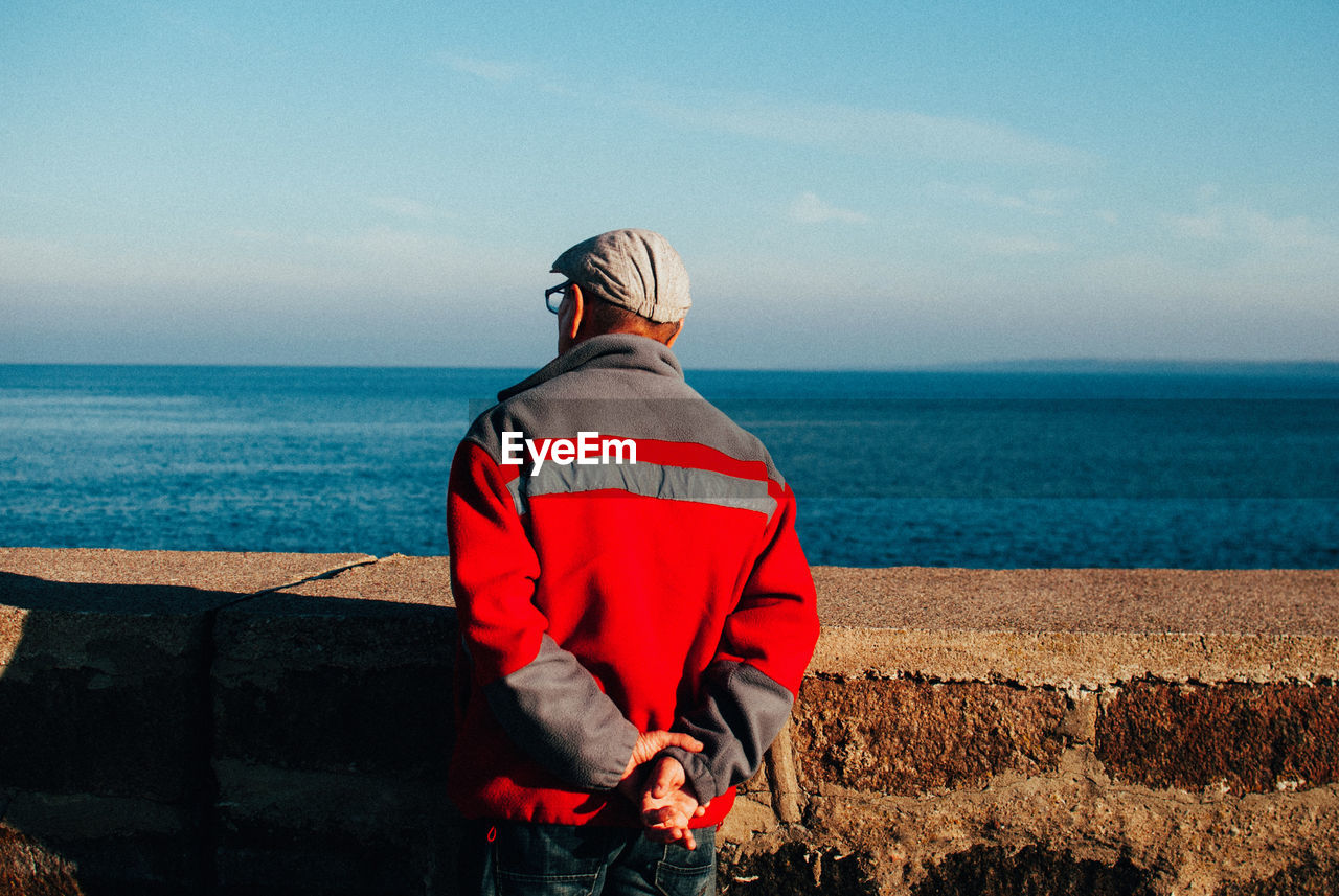 REAR VIEW OF PERSON LOOKING AT SEA AGAINST SKY