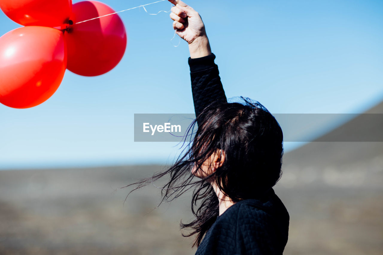 Side view of young woman holding balloons at beach