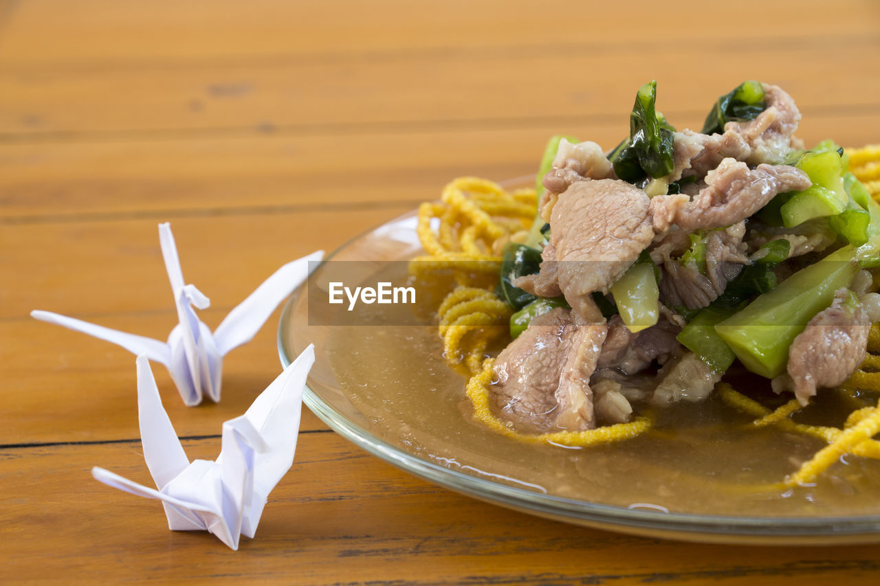 Close-up of meat salad on fried noodles in plate by origami at table