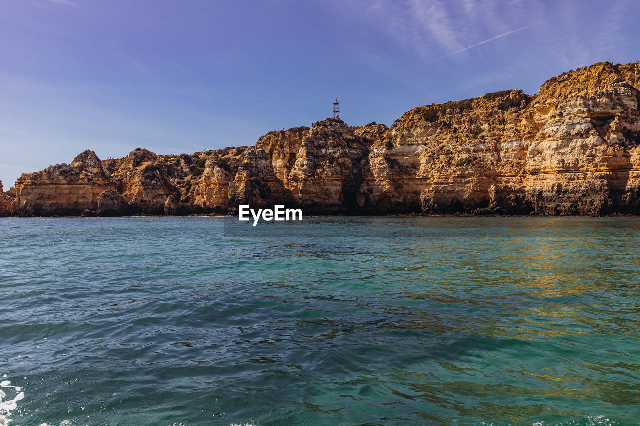 Rock formations by sea against blue sky