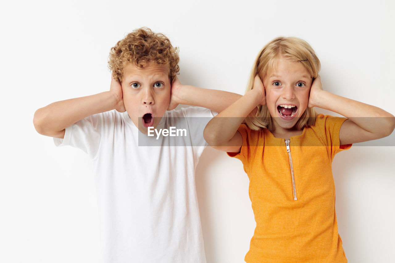 Portrait of sibling covering ears against white background