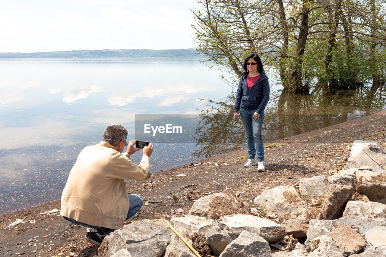 MAN PHOTOGRAPHING WHILE STANDING BY LAKE