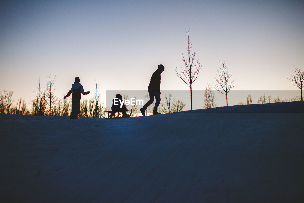 Silhouette people on snow covered land against sky during sunset