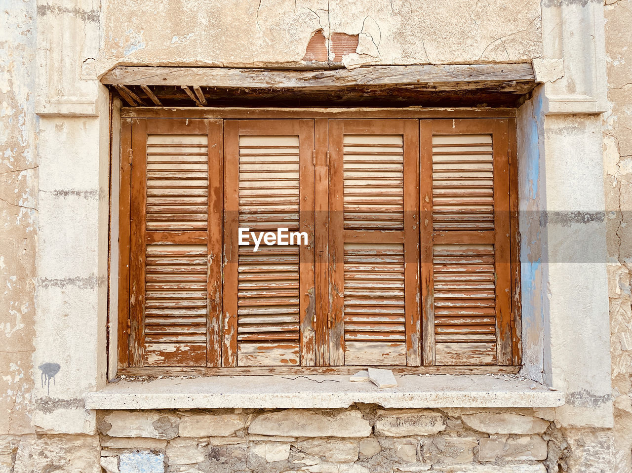 Old rustic weathered wooden window closed shutters on stone wall