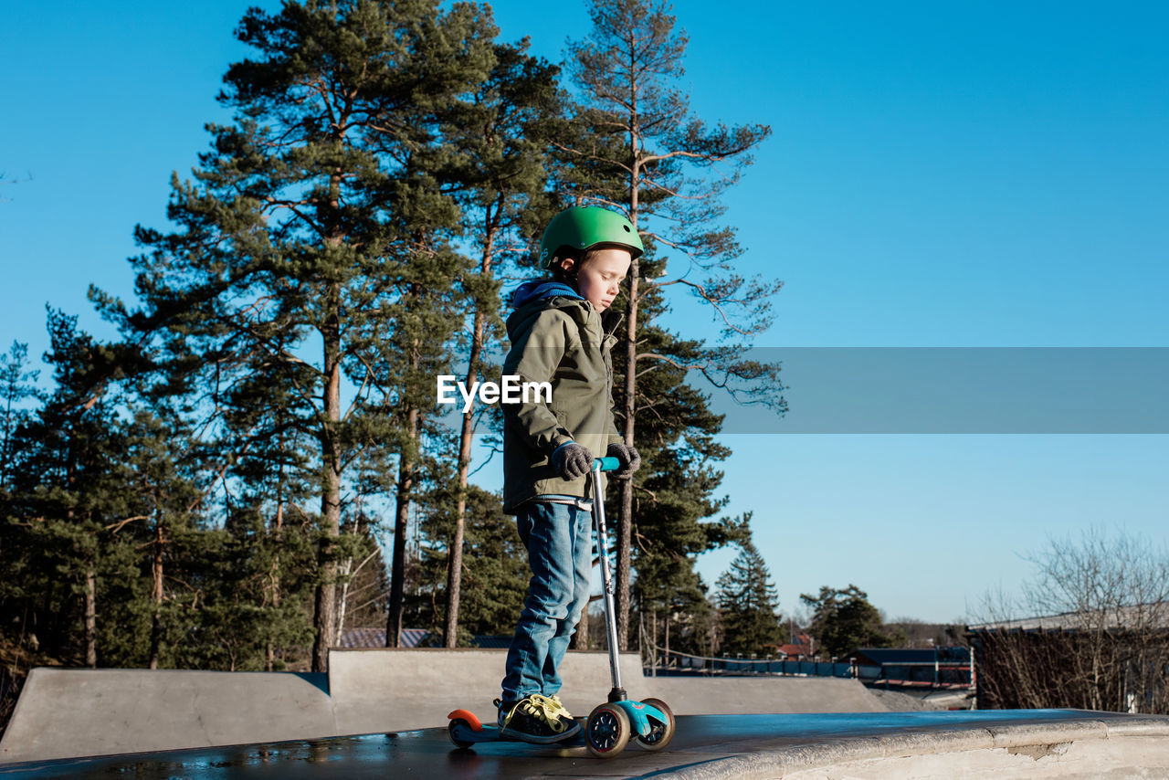 Boy standing on his scooter in a skatepark in the sunshine