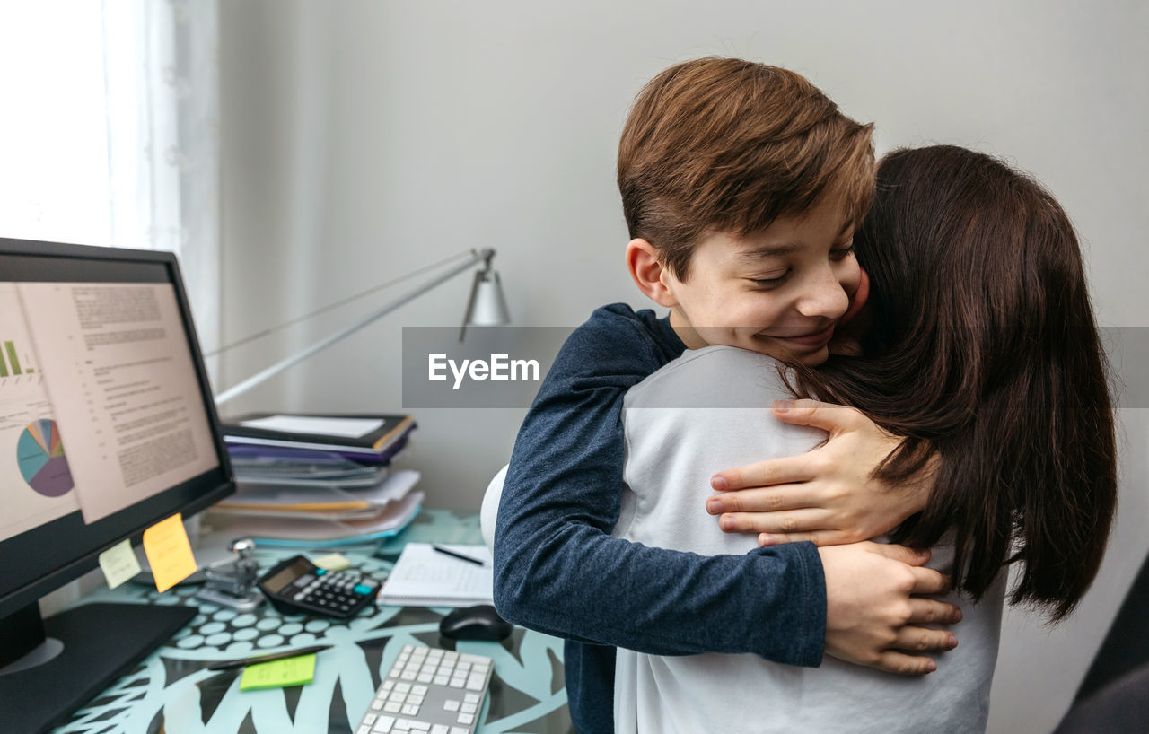 Mother and son hugging while she telecommutes from home