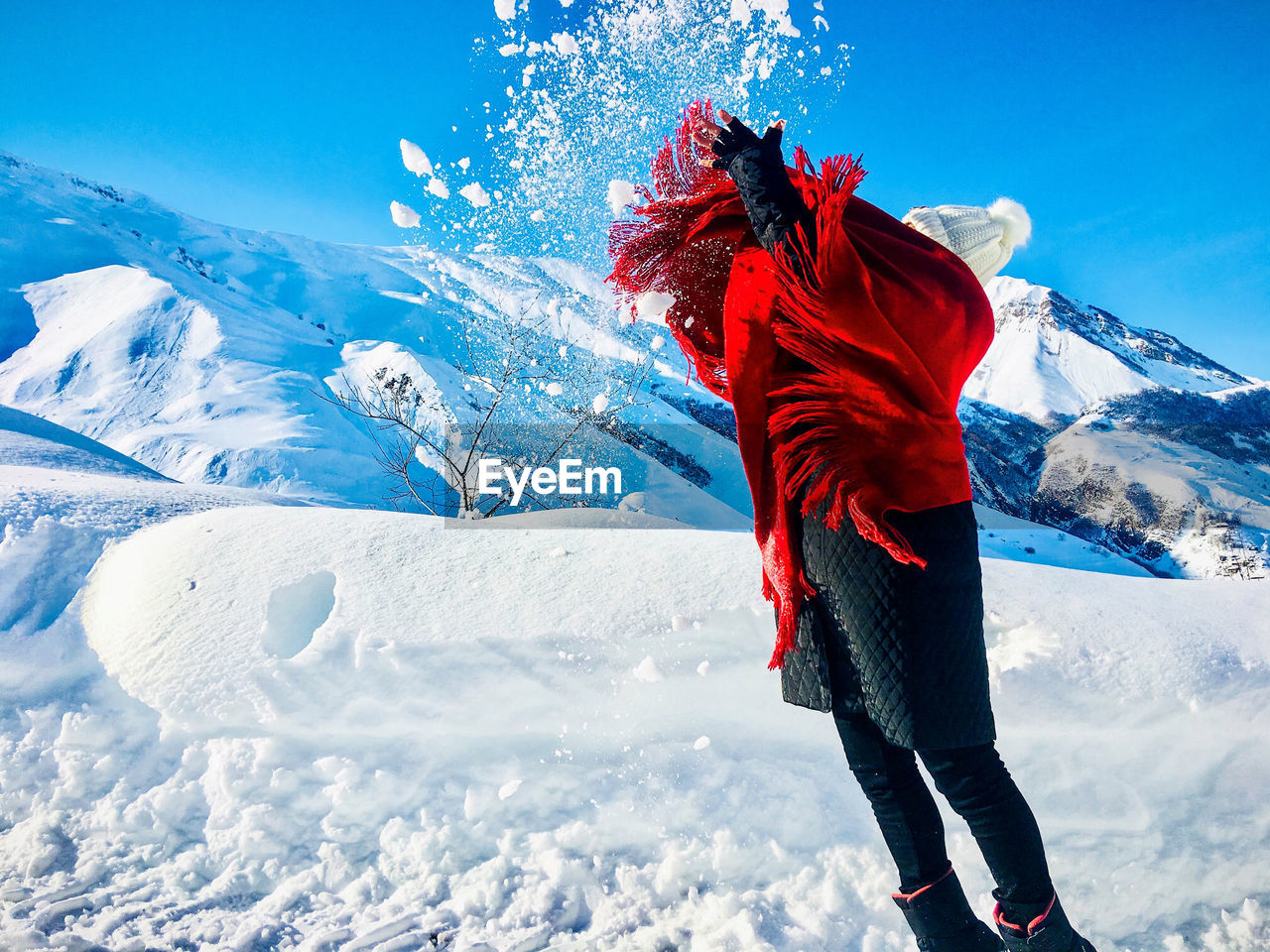 Woman playing with snow on snowcapped mountain against sky