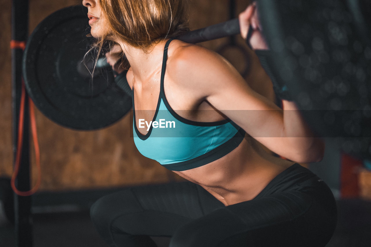 Midsection of young woman lifting weights in gym