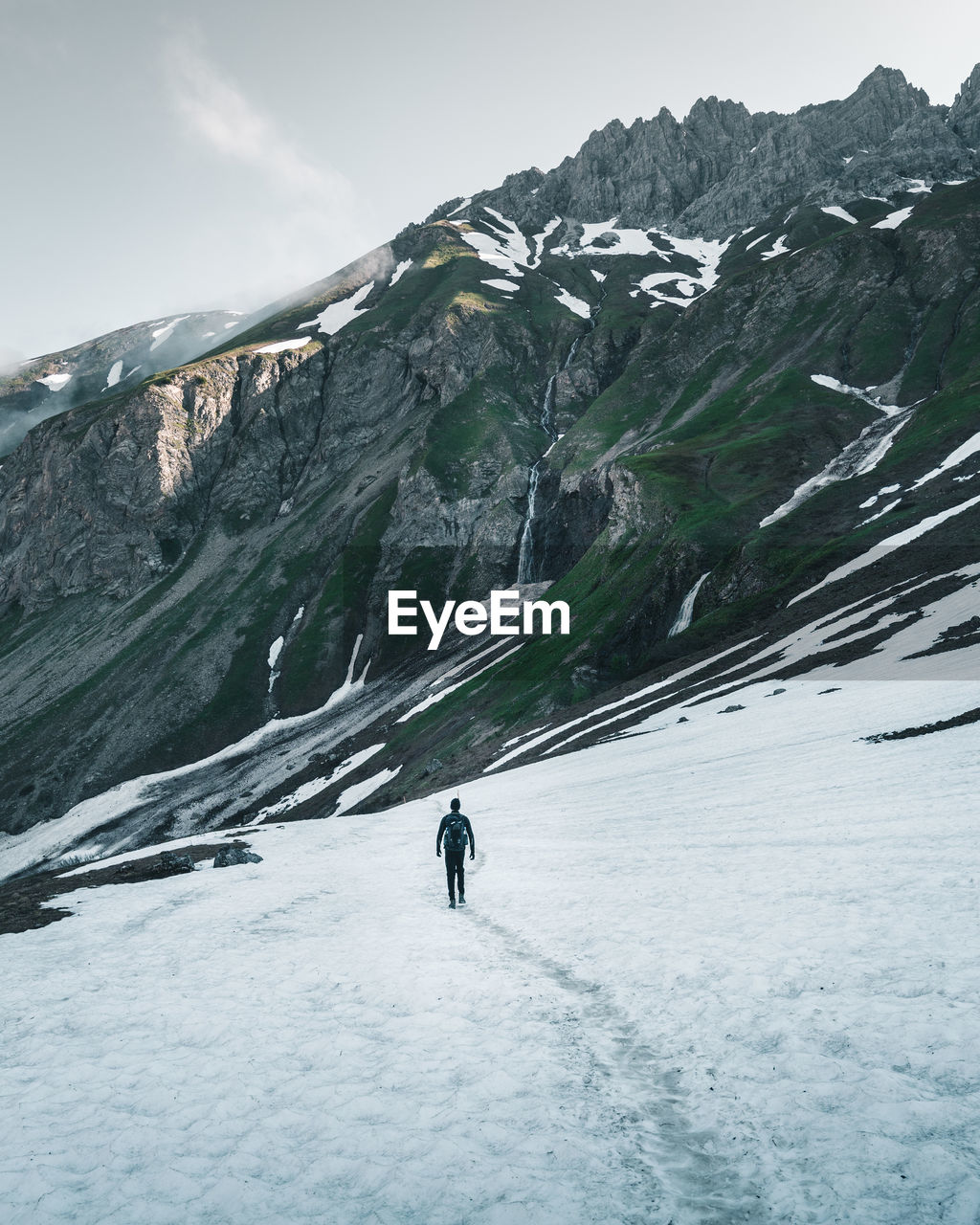 Rear view of man walking on snow covered land against sky