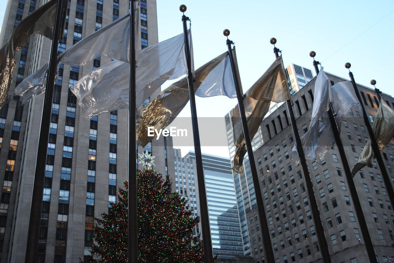 Low angle view of flags by modern buildings in city against clear sky