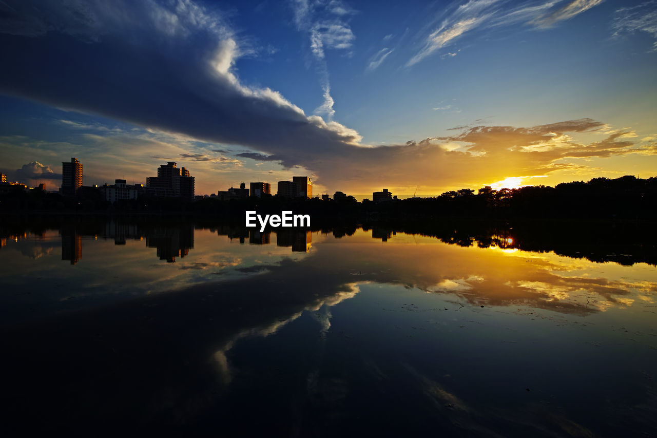 Silhouette buildings by lake against sky during sunset