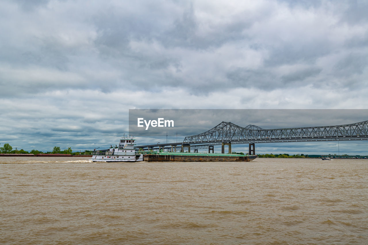 Tugboat pushing barge on the muddy mississippi river. crescent city bridge in background