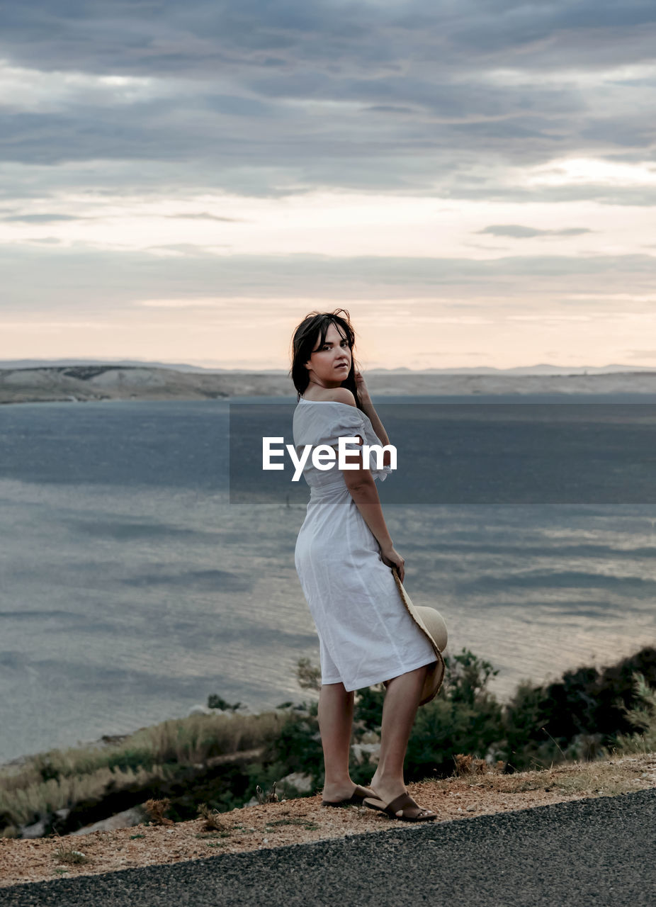  portrait of beautiful young woman standing on coast above sea. summer, travel, wanderlust.