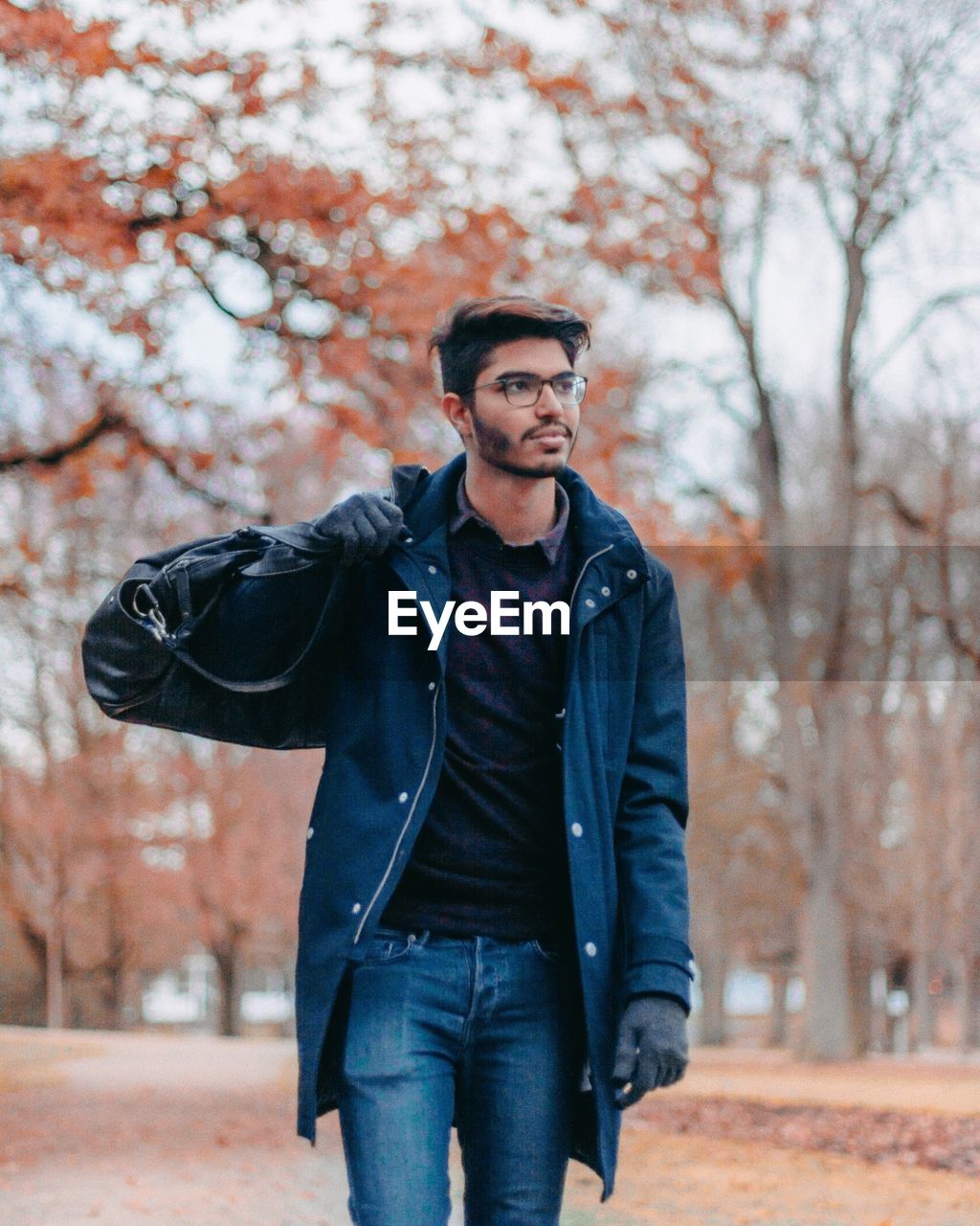 Young man walking with luggage in park during autumn