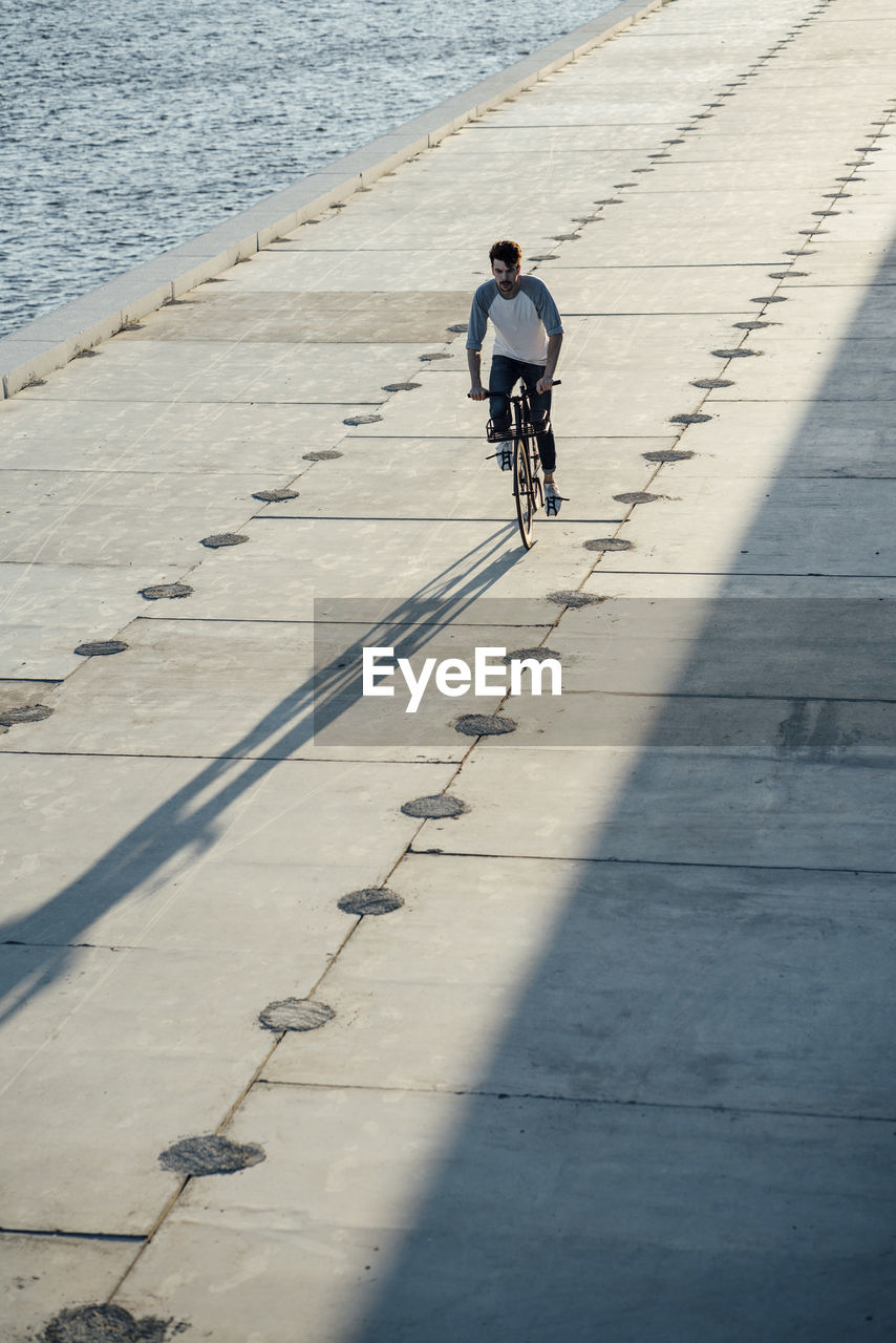 Young man riding bike on waterfront promenade at the riverside