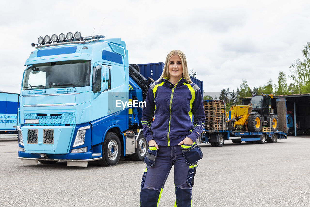 Blond female truck driver standing next to truck