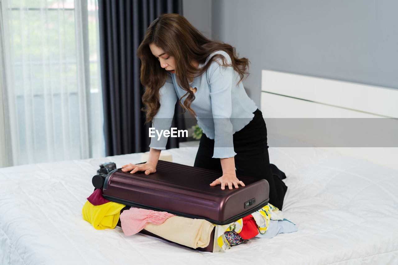 side view of young woman using mobile phone while sitting on bed at home