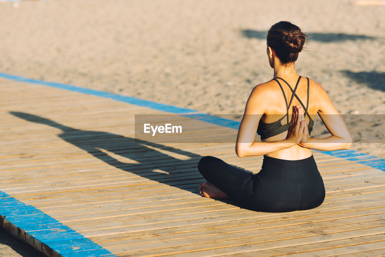 Rear view of mid adult woman exercising on boardwalk at beach