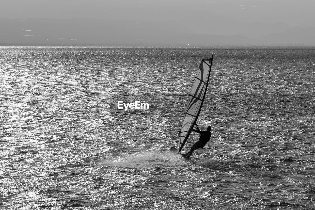 water, black and white, sea, nature, monochrome photography, monochrome, wave, sky, coast, wind, beauty in nature, scenics - nature, day, horizon over water, shore, horizon, land, surfing, ocean, leisure activity, waterfront, wind wave, one person, tranquility, outdoors, sports, lifestyles, men, tranquil scene, non-urban scene, windsurfing, sunlight, water sports, beach, black, adventure