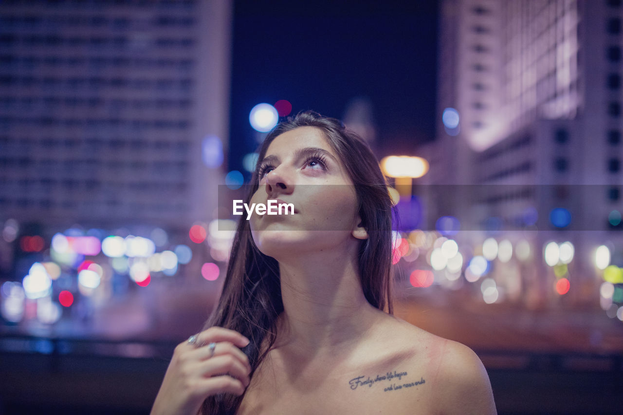 Young woman looking up at illuminated city