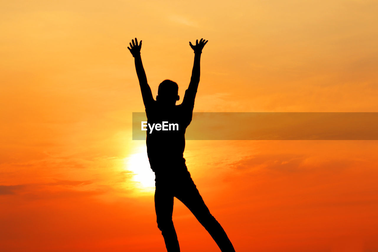 Silhouette man with arms raised standing against orange sky