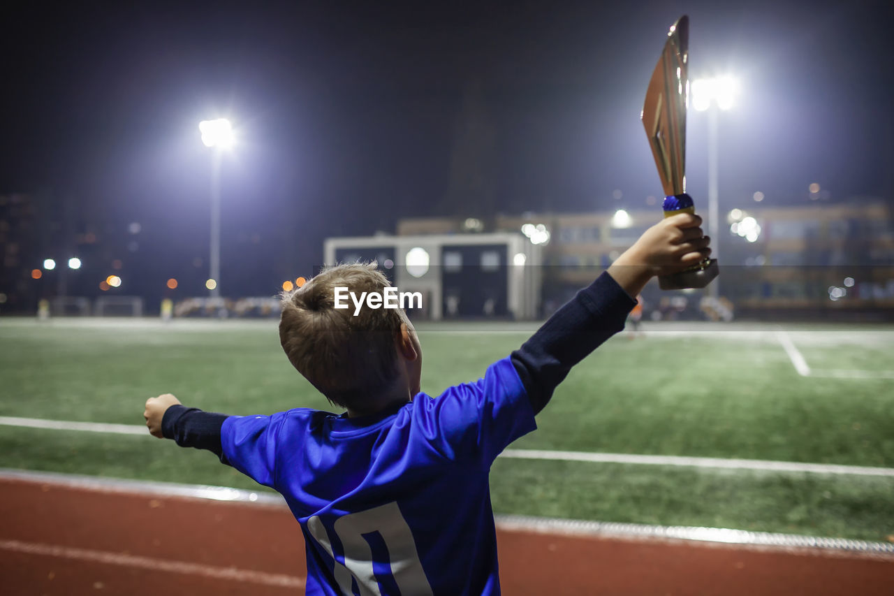 Young soccer player in blue jersey with ten number raising a trophy after the winning goal