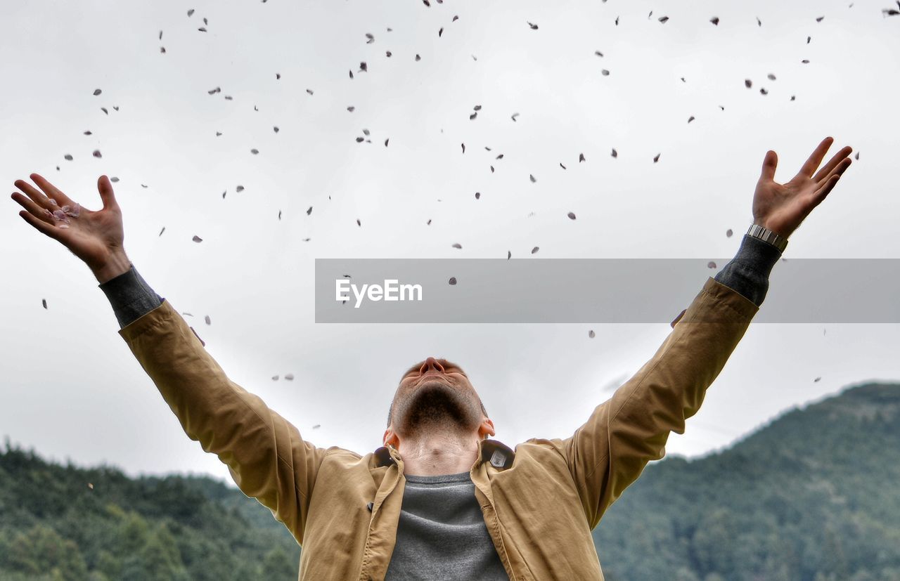 Man throwing petals against sky