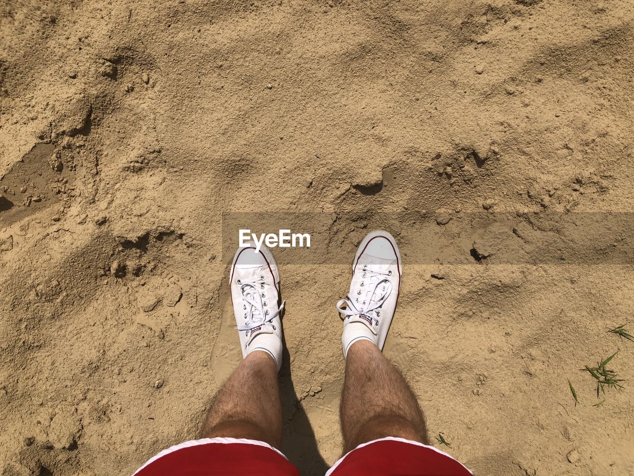 LOW SECTION OF MAN STANDING ON SANDY BEACH