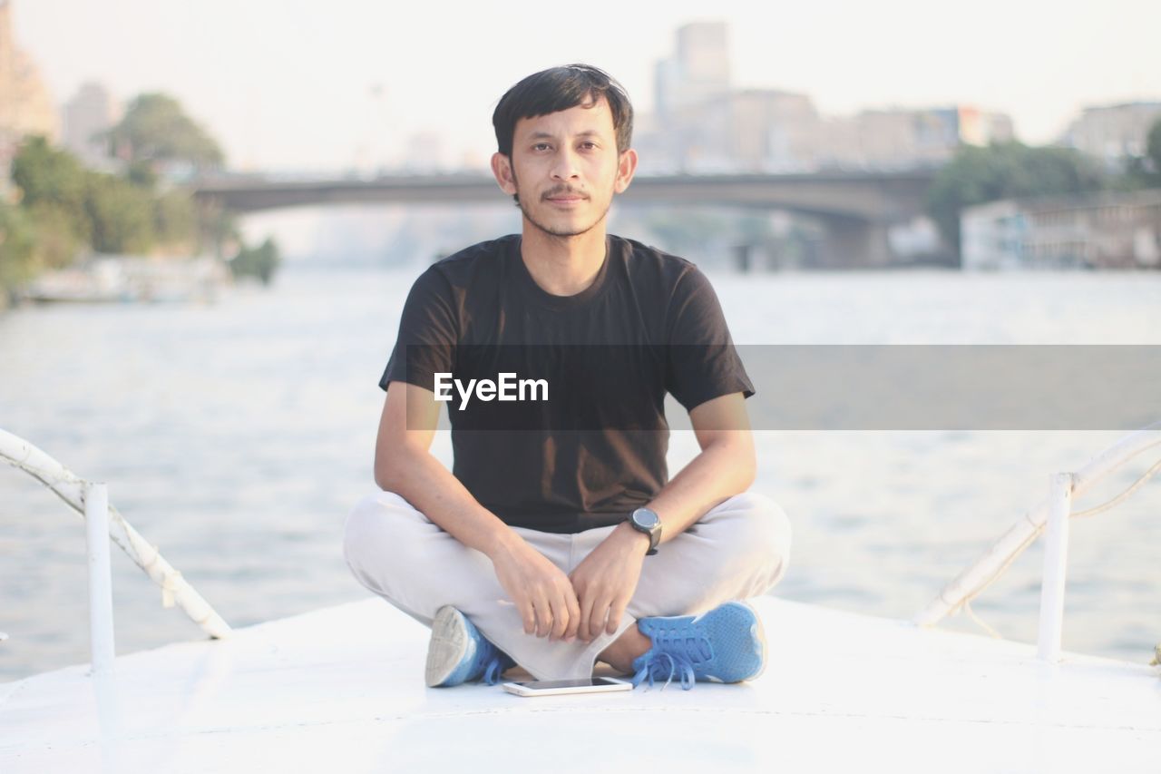 PORTRAIT OF YOUNG MAN SITTING BY WATER