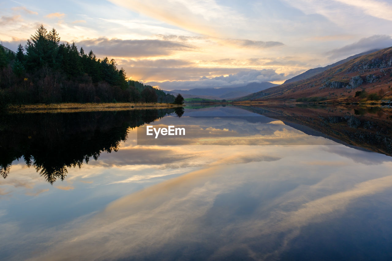 reflection, water, sky, scenics - nature, cloud, nature, beauty in nature, lake, morning, environment, tranquility, landscape, mountain, tranquil scene, dawn, tree, sunrise, no people, plant, land, reservoir, body of water, travel destinations, mountain range, travel, outdoors, idyllic, forest, sun, non-urban scene, sunlight, twilight, reflection lake, dramatic sky, tourism, blue