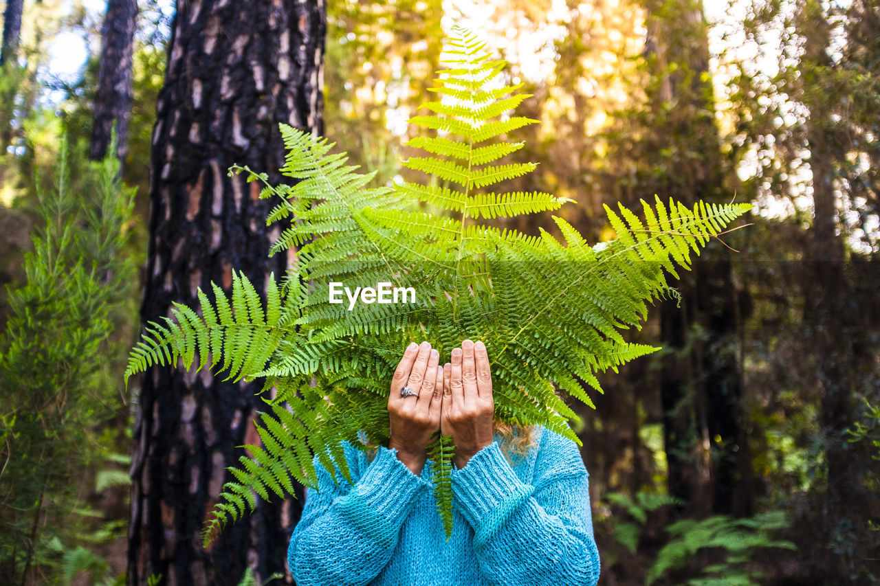 Mature woman holding leaves standing against trees